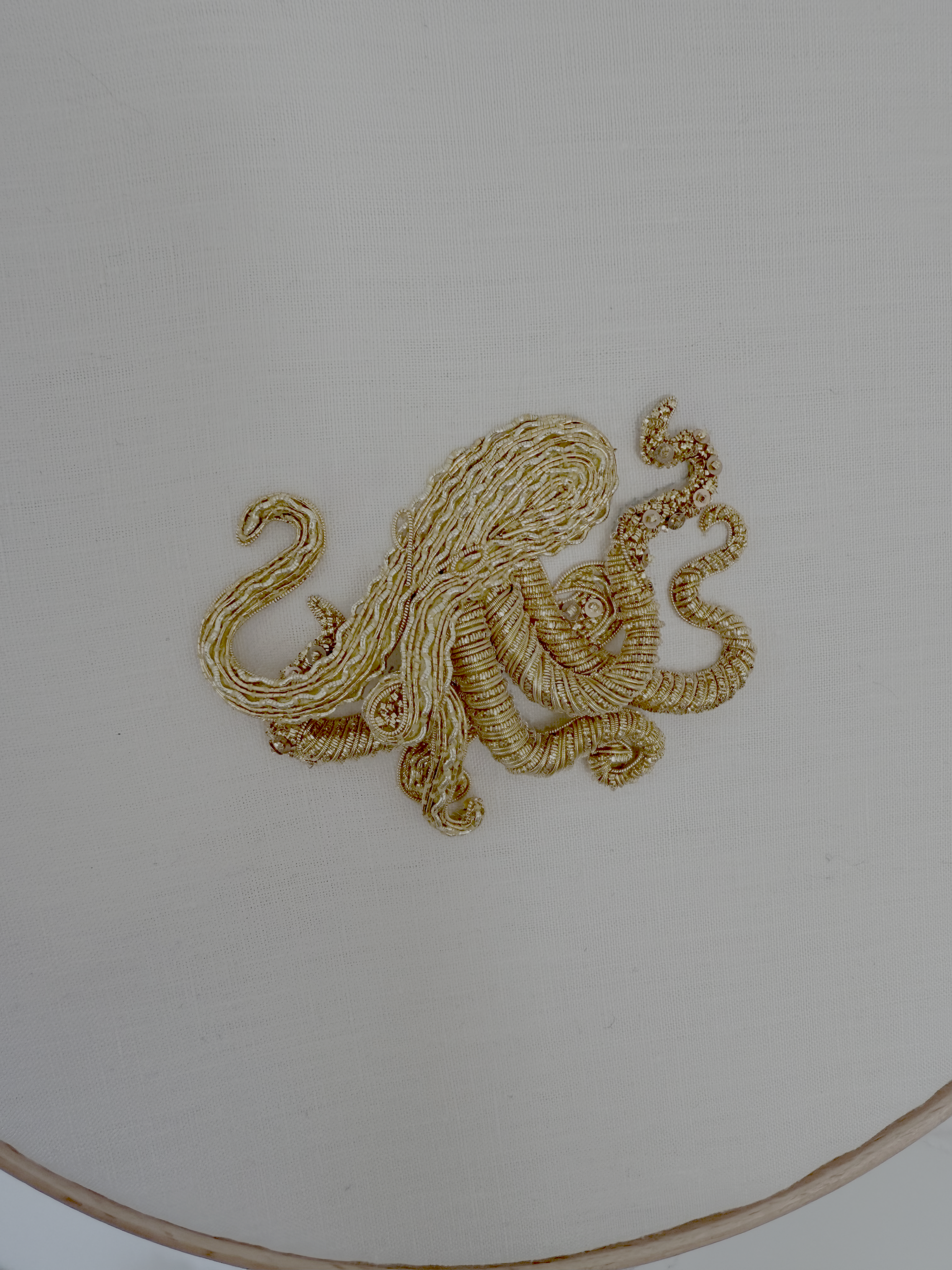 An octopus worked in goldwork embroidery, its tentacles curling across pale linen in gold purl and seed beads.